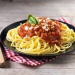 a plate of spaghetti with sauce and basil on a napkin